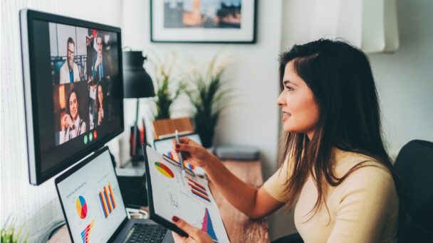 A woman working on her laptop in front of a painting on a monitor screen.
